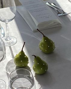 three pears sitting on a table with wine glasses and silverware next to them