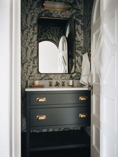 a bathroom sink with a mirror above it next to a wallpapered wall and door