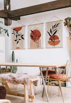 three paintings hang on the wall above a dining room table