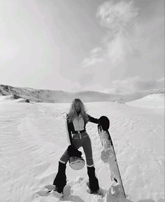 a woman standing in the snow holding a snowboard