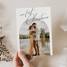 someone holding up a christmas card with the image of two people kissing on a pier