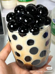 a hand holding a glass filled with black and white desserts on top of a table