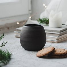 a black vase sitting on top of a table next to some cookies and a candle