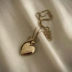 a gold heart shaped pendant on a white satin surface with a chain attached to it