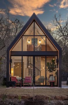 a small house with lots of windows and furniture in front of the window is lit up at night