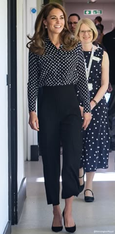 a woman in black and white polka dot shirt and pants walking down a hallway with other people