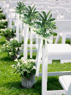 rows of white chairs with plants in them on the grass at an outdoor wedding ceremony