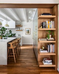 an open kitchen and dining room with wood flooring, white walls and wooden shelves