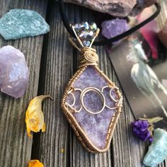 a wire wrapped pendant is sitting on a wooden table next to some rocks and flowers