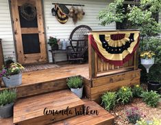 a wooden porch with flowers and plants on the steps next to it is decorated with an american flag