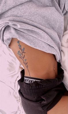 a woman's stomach with a tattoo on her lower back and the bottom part of her body covered by a blanket