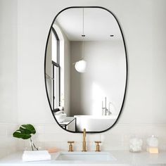 a bathroom sink with a large oval mirror above it and a plant in the corner