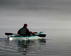 a man is paddling his kayak in the calm water on a foggy day