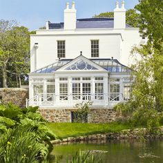 a large white house sitting on top of a lush green field next to a lake