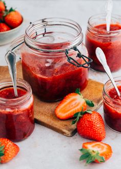 three jars filled with strawberry jam sitting on top of a wooden cutting board next to strawberries