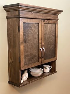 a wooden cabinet with two plates and cups on it's shelf next to a wall