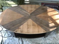 a round wooden table sitting on top of a sheet of plastic next to a window