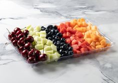 an assortment of fruit in a plastic tray on a marble counter top with cherries and watermelon