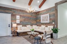 a living room with wood paneled walls and white furniture in the center, along with a chandelier