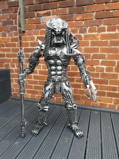 a statue of an alien holding a large knife and wearing metal armor, standing on a deck