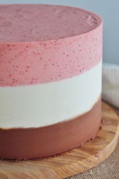 a cake with pink and white frosting on a wooden platter next to a napkin