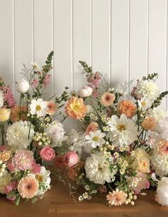 several different types of flowers are arranged on a wooden table in front of a white wall