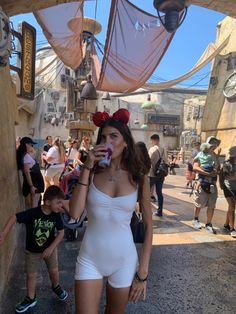 a woman in a white bodysuit drinking from a cup while standing next to a little boy