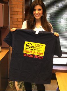 a woman holding up a black t - shirt in an office