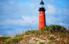 a red light house sitting on top of a hill next to tall grass and weeds