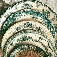 four green and white plates stacked on top of each other in front of a lace covered tablecloth