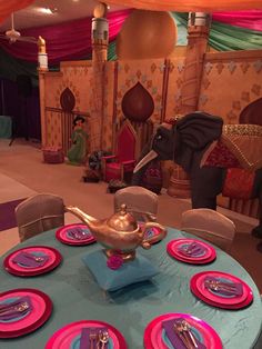 a table set with pink and blue plates, silverware and an elephant figurine