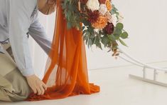 a man kneeling down next to a vase with flowers on it and an orange scarf