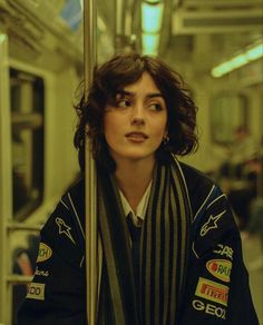 a woman sitting on a subway train with her scarf draped around her neck and looking off into the distance