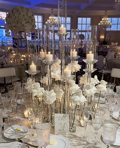 a table is set with white flowers, candles and place settings for an elegant dinner