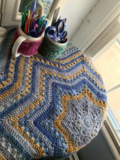 a crocheted table cloth with mugs and pencils on it next to a window sill