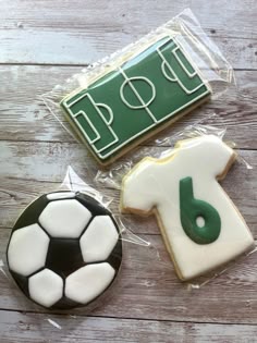 three decorated cookies in the shape of soccer shirts and a t - shirt are sitting on a wooden table