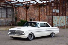 an old white car parked in front of a rusty building