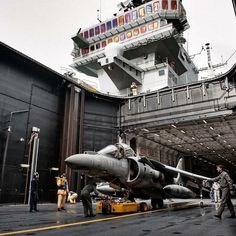 an airplane is parked on the deck of a ship as people stand around it and watch