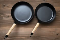 two black frying pans sitting on top of a wooden table next to each other