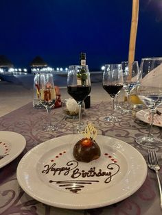 a plate with a piece of cake on it sitting on a table next to wine glasses