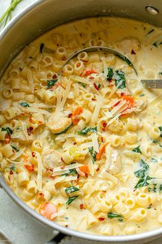 a pot filled with pasta and vegetables on top of a table next to a spoon