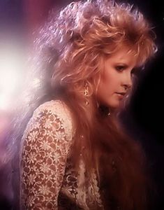 a woman with long blonde hair standing in front of a dark background and looking off to the side