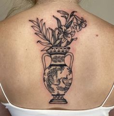 a woman with a tattoo on her back has a vase full of flowers in it