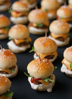 mini burgers with toothpicks in them on a black tableclothed surface