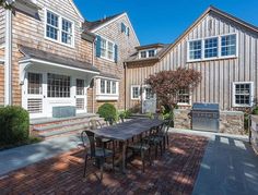 an outdoor dining table and grill in front of two large wooden houses with brick patios