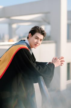 a young man wearing a graduation robe and holding his hands out