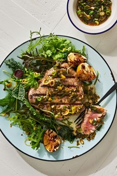 a white plate topped with meat and vegetables next to a bowl of sauce on top of a table