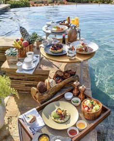 an outdoor table with food and drinks near the water's edge, next to a swimming pool