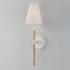 a white wall mounted light with a lamp shade on it's side and a wooden stick in the corner