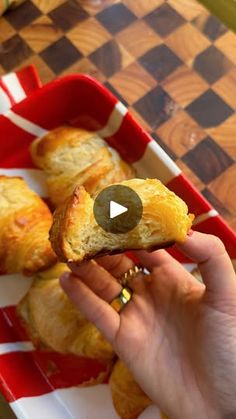 a person holding up a piece of bread in front of some other pastries on a red and white checkered tray